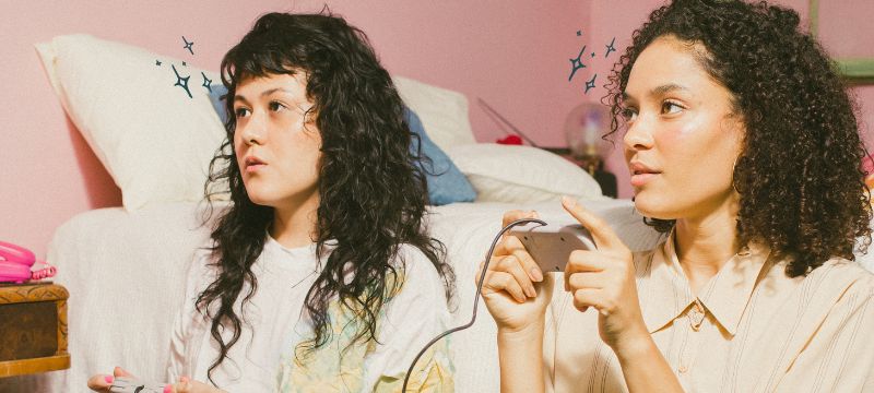 Two women with long black hair holding video game controllers looking to the left