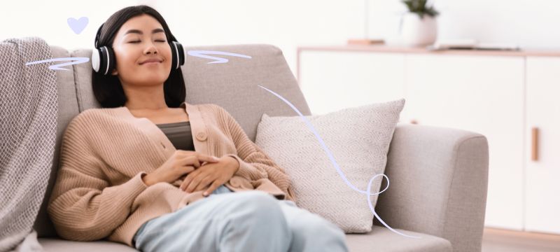 Woman sitting on a couch with headphones on and her eyes closed, smiling