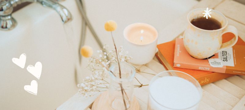 A stack of orange books, a cup of tea and a few candles rest on a board over a cream coloured bathtub