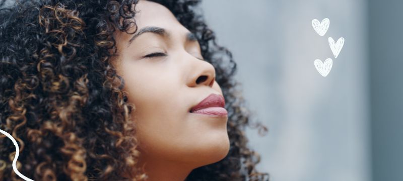 Close up of a woman with black curly hair softly smiling with her eyes closed