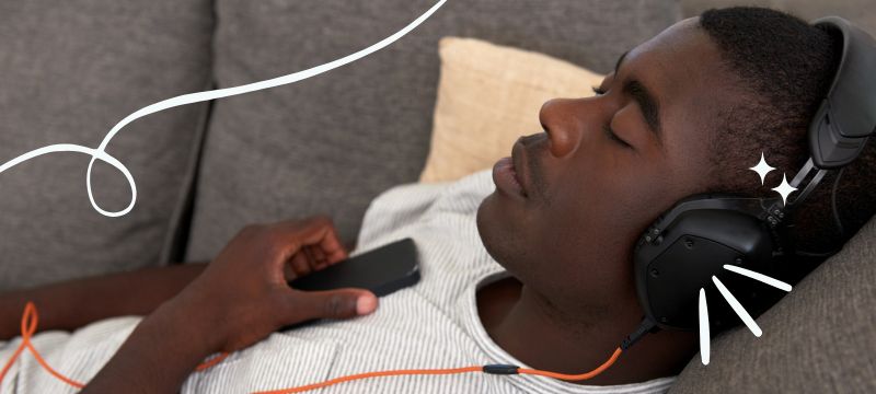 Side view of man lying on couch with eyes closed and headphones on holding a phone