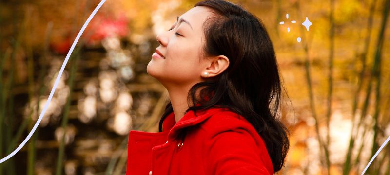 Woman with black hair wearing a red coat smiles softly with her eyes closed