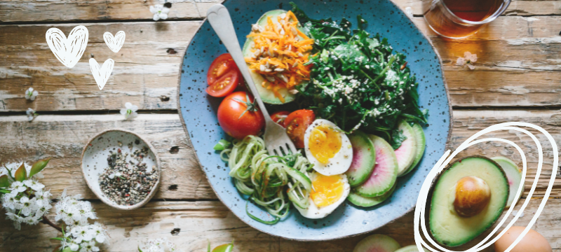 Blue plate of salad and an avocado on a wooden table