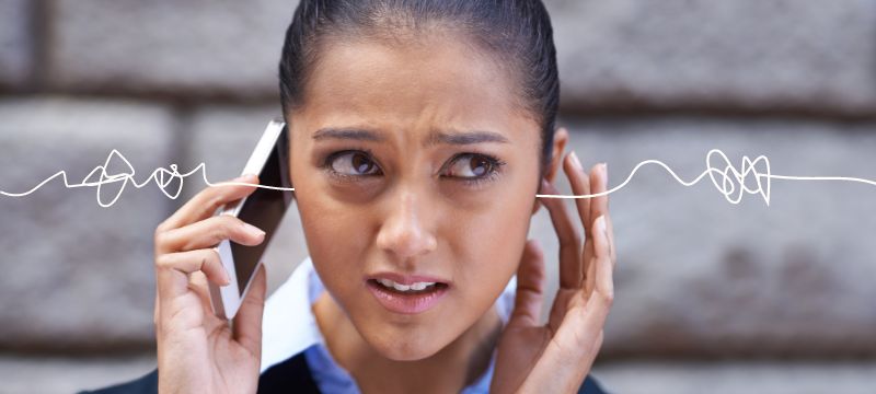 Woman on a phone with a furrowed brow and her fingers in her ears with squiggly illustrated lines on either side of her ears